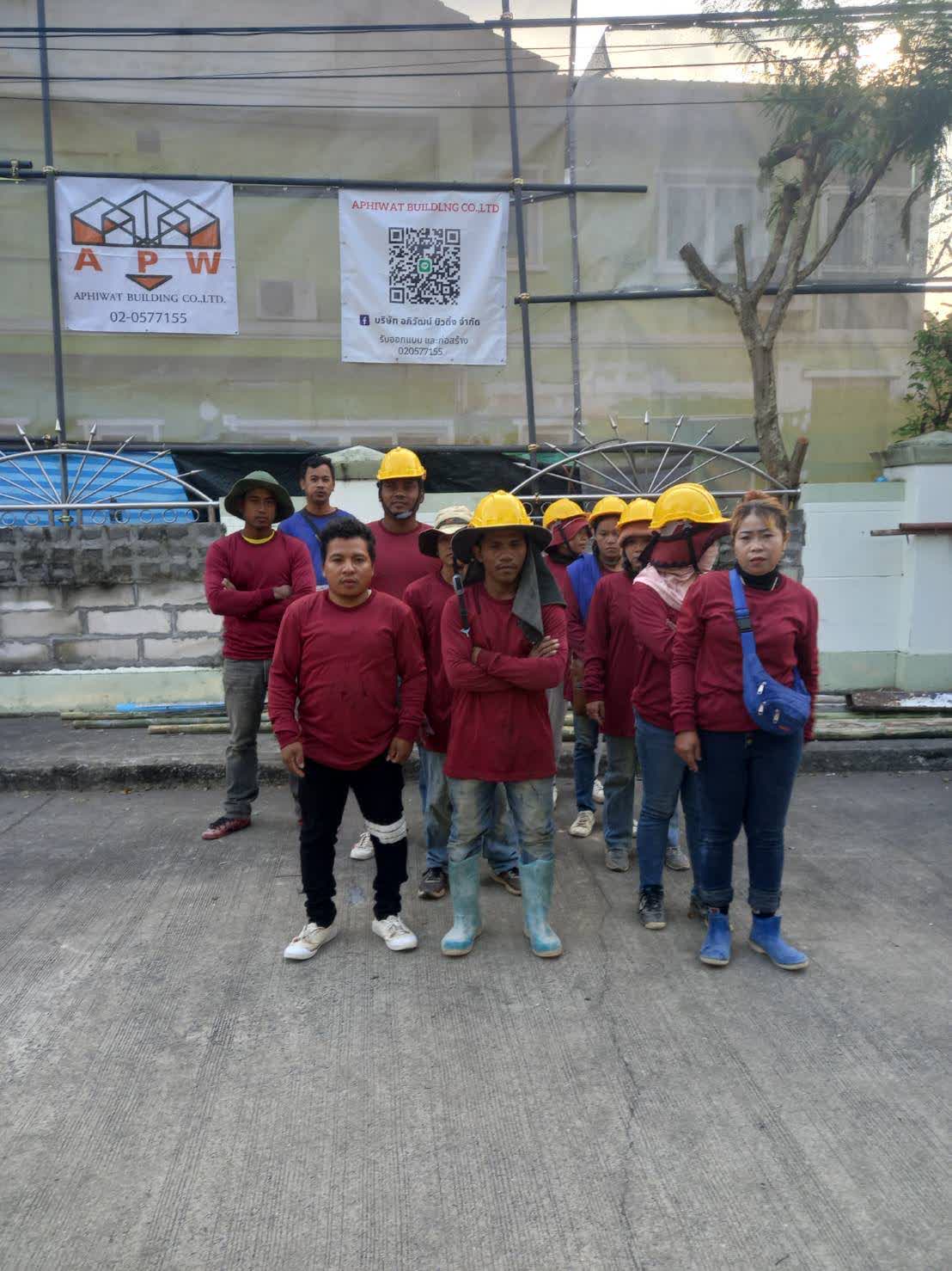 ทีมช่างประจำโครงการพร้อมหมวกนิรภัยหน้าป้ายโครงการ APW