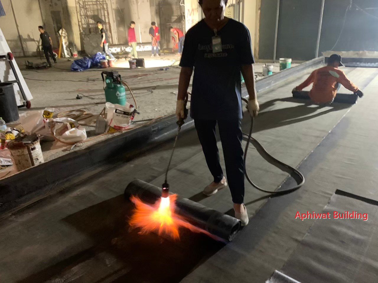ลนไฟรีดแผ่นกันซึมให้ติดพื้นตลอดแนว — งานช่วงกลางคืนหลังห้างปิด