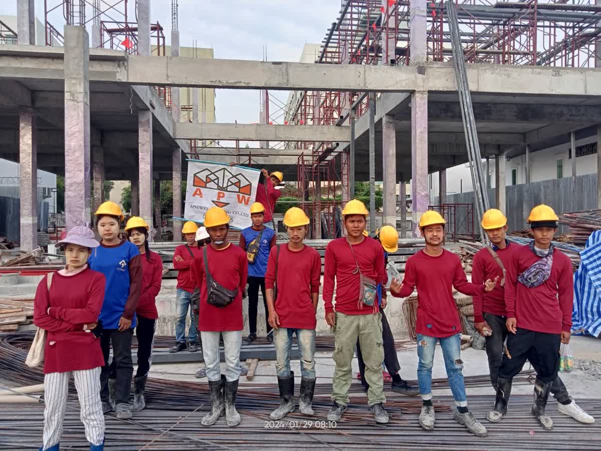 ทีมช่างประจำโครงการถ่ายรูปหมู่หน้าโครงสร้างอาคารพร้อมป้าย APW